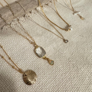 Gold necklaces with various pendants on a textured surface